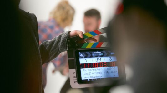 A clapper on focus and a talent with talent manager in the background