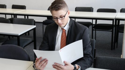 male person wearing black eyeglasses and holding whilte folder