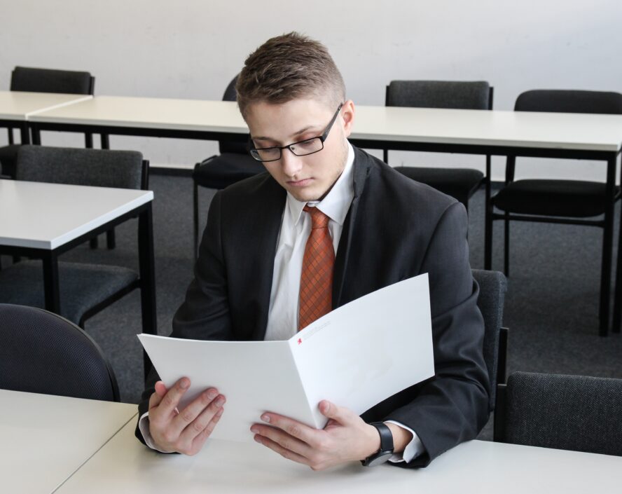 male person wearing black eyeglasses and holding whilte folder