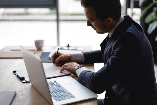 a man writing some notes with laptop open on the table