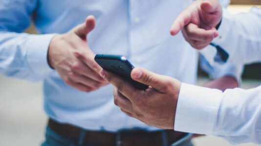 a man holding a mobile phone showing it to another person