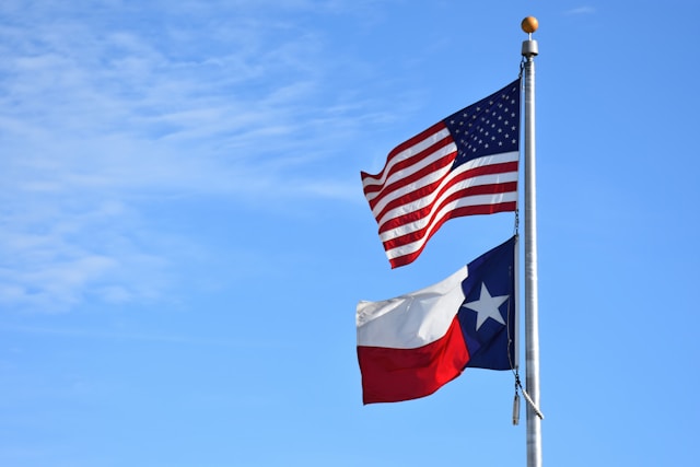 US flag and Texas State Flag displayed blowing in the breeze against a beautiful Texas sky.